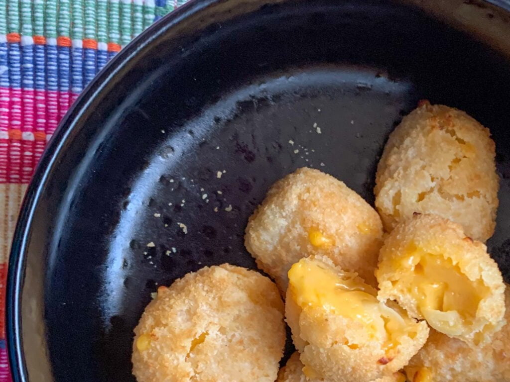 Oblong mac and cheese bites In a black bowl with a pink plaid background 