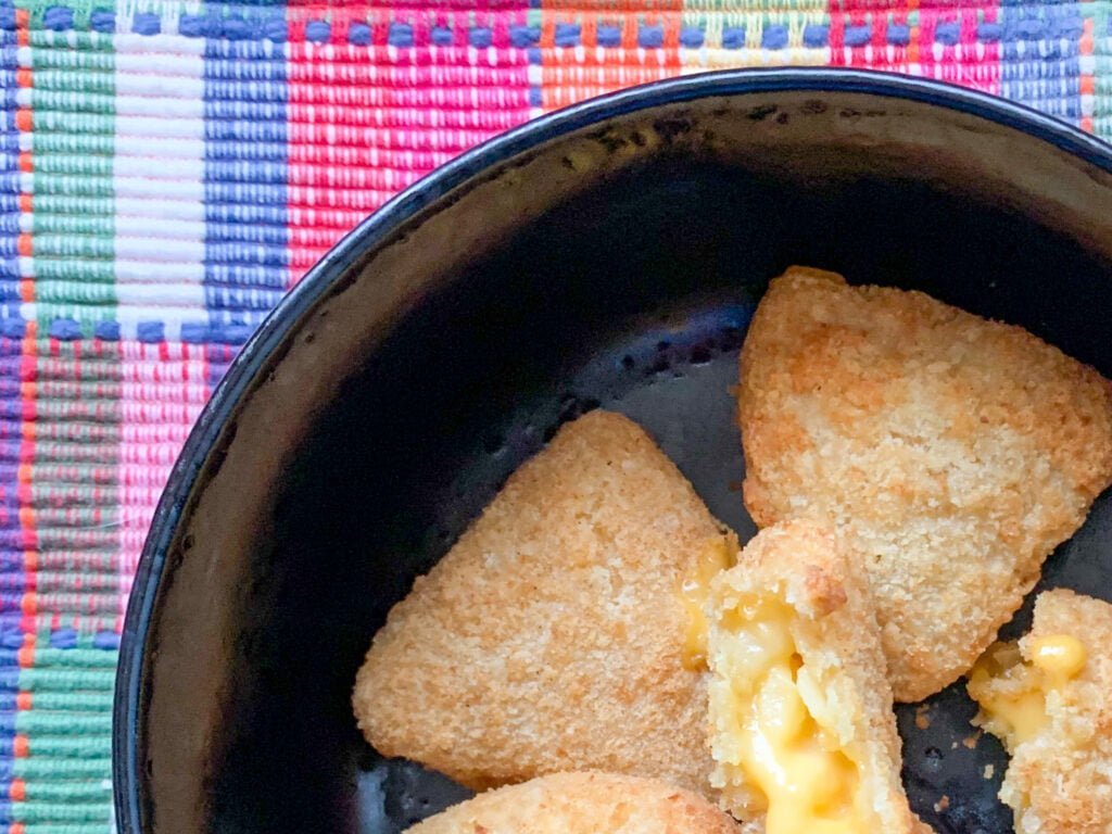 Triangular mac and cheese bites in a black bowl with a pink plaid background 