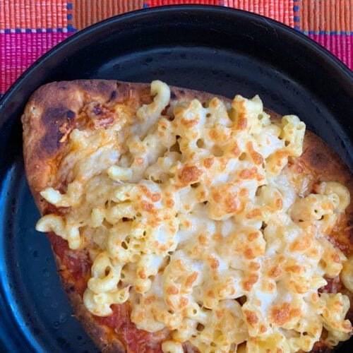 Mac and cheese on a naan crust in a black plate with a pink plaid background