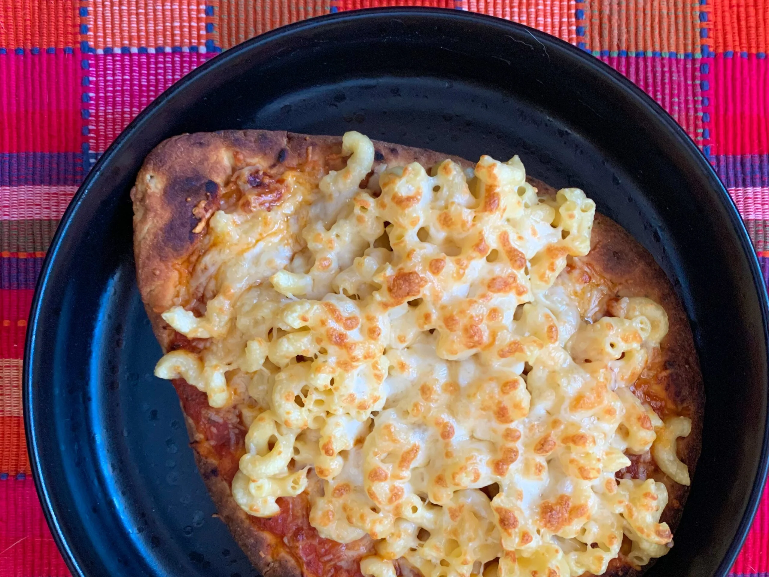 Mac and cheese on a naan crust in a black plate with a pink plaid background