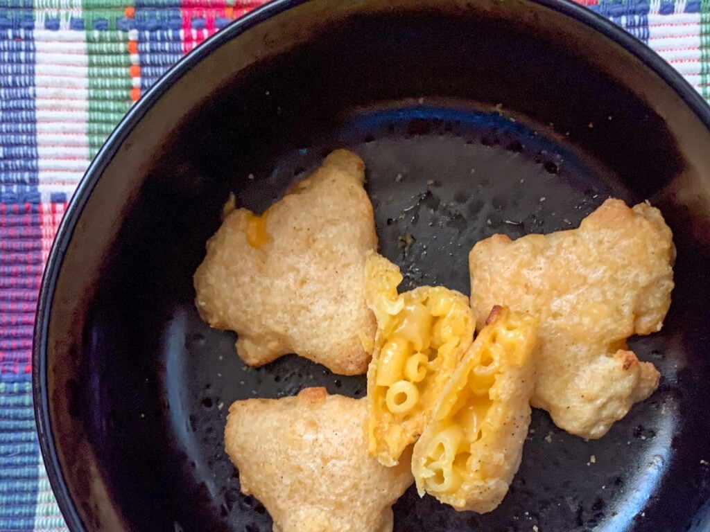 Triangle shaped fried mac and cheese bites in a black bowl on a pink plaid background 