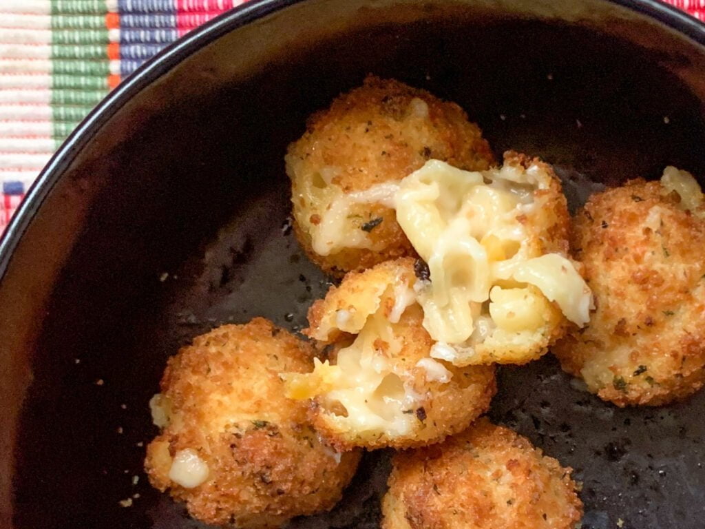 Round mac and cheese bites in a black bowl with a pink plaid background 