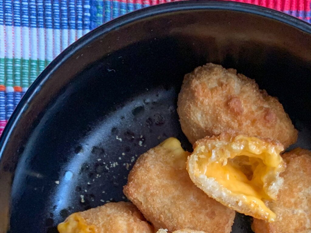 Oblong mac and cheese bites in a black bowl with a pink plaid background 