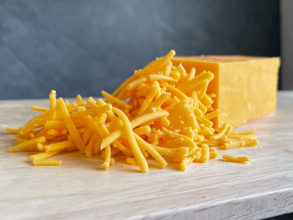 A solid block of cheddar cheese sitting behind a pile of shredded cheddar.