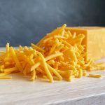 A solid block of cheddar cheese sitting behind a pile of shredded cheddar.