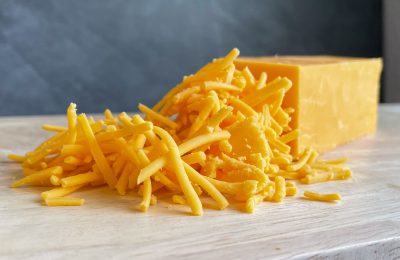 A solid block of cheddar cheese sitting behind a pile of shredded cheddar.